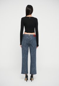 Black cropped long-sleeve top paired with blue textured wide-leg pants featuring a shimmering pattern. Black high heels complete the look.