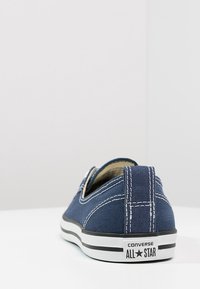 Baskets slip-on en toile bleu marine avec des coutures blanches, semelle en caoutchouc et double bande noire, avec un logo au niveau du talon.