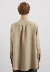 Beige linen shirt with a loose fit, long sleeves, single back pleat, and buttoned cuffs. Smooth texture, curved hem.