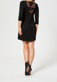 Svart klänning med spetsbakdesign, ¾-ärmar, figursydd form och mjuk textur. Kombination med svarta ankelstövlar med stilettklackar.