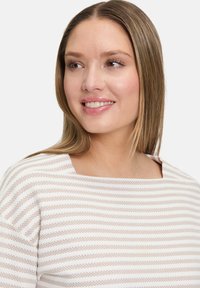 Cremegestreifter Pullover mit quadratischem Ausschnitt, weichem Material und lockerer Passform. Die Streifen wechseln sich zwischen hellbeige und cremefarben ab.