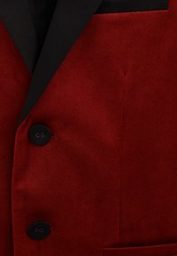 Czerwony żakiet z teksturowanym wzorem w jodełkę, czarnymi klapami, dwiema czarnymi guzikami i kieszenią na piersi.