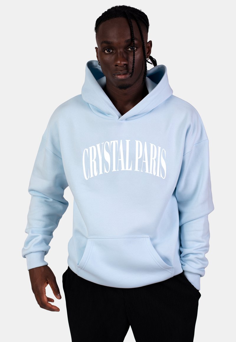 Hoodie azzurro chiaro con tasca frontale, maniche ampie e testo "CRYSTAL PARIS" in bianco. Tessuto morbido con una texture liscia.