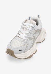 Zapatilla de running ligera en blanco y beige. Presenta paneles de malla, un collar acolchado y una suela texturizada con acentos grises. Los cordones se ajustan de manera segura.
