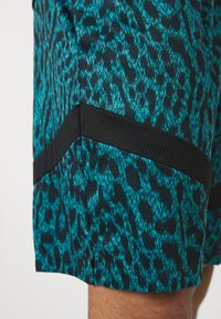 Shorts à motifs teal et noir présentant un design de léopard, un tissu texturé et un accent en mesh noir le long de l'ourlet.