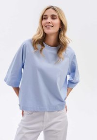Jasnoniebieska bawełniana koszulka z okrągłym dekoltem, krótkimi rękawami i luźnym krojem. Gładka faktura z subtelnymi detalami zszycia.