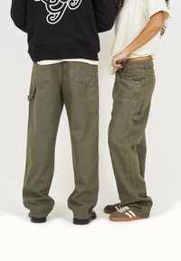 Grüne Cargo-Hosen mit lockerer Passform, die mehrere Taschen, genähte Details und einen strukturierten Stoff aufweisen. Kombiniert mit lässigen Sneakern.