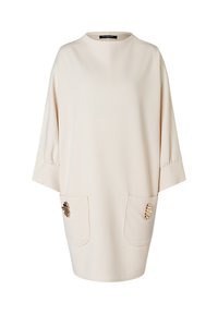 Cremefarbenes Kleid mit langen Ärmeln und Rundhalsausschnitt, ausgestattet mit zwei vorderen Taschen, die mit goldenen Hardware-Akzenten verziert sind. Glatte, weiche Stoffstruktur.