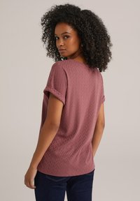 Haut bordeaux à manches courtes avec un motif en zigzag texturé, col rond et manches retroussées. Porté avec un jean bleu foncé.