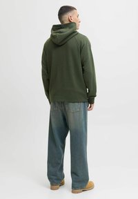 Sweat à capuche vert olive avec une finition texturée, doté d'une capuche avec cordon de serrage. Assorti à un jean bleu délavé à coupe ample et des chaussures beiges.