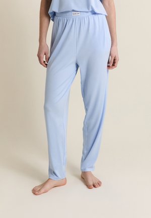 Osoba stojąca na boso, ubrana w jasnoniebieskie luźne spodnie i pasujący top z napisem "Zdrowa dusza" na pasku.