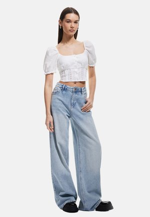 Top corto bianco con maniche a sbuffo e dettagli con bottoni, abbinato a jeans in denim azzurro chiaro a gamba larga e scarpe con plateau nere.