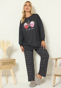 Czarny longsleeve z nadrukiem "Hot Choc o'clock". Pasujące spodnie mają wzór w serca. Miękka tkanina, luźny krój, w połączeniu z szarymi kapciami.