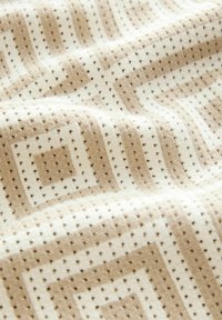 Beiger und cremefarbener Stoff mit Muster aus Quadraten und Punkten; weiche Textur mit leichtem Glanz, geeignet für Polster oder Vorhänge.