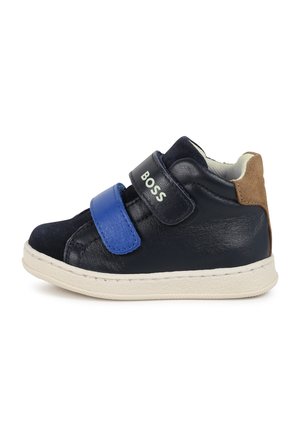 Baskets montantes en cuir bleu marine avec une sangle Velcro bleue, semelle en caoutchouc blanche et accent en suède marron au talon. Présente un logo en relief.