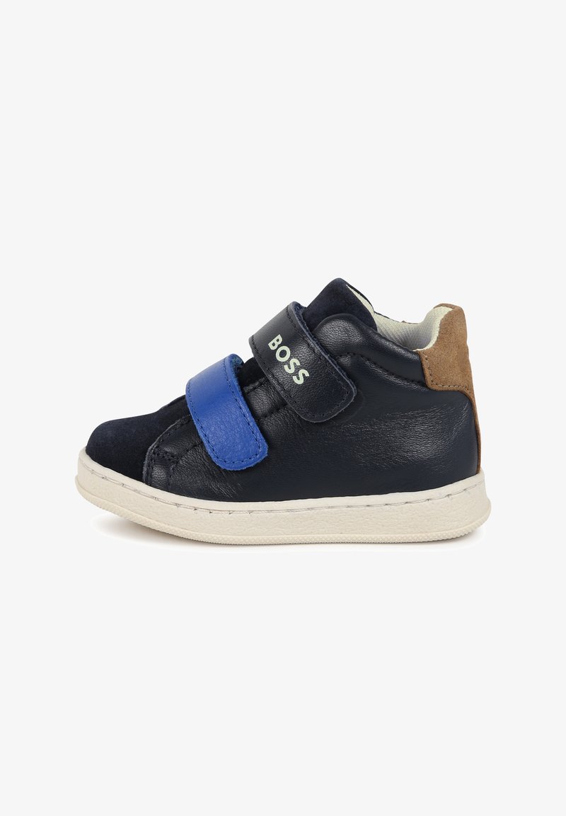 Baskets montantes en cuir bleu marine avec une sangle Velcro bleue, semelle en caoutchouc blanche et accent en suède marron au talon. Présente un logo en relief.