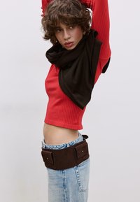 Rdeča rebrasta kratek top, rjava ruta, modre visokokotne kavbojke in rjava semiš torbica z dvema sprednjima žepoma; gladke teksture in oprijeta zasnova.