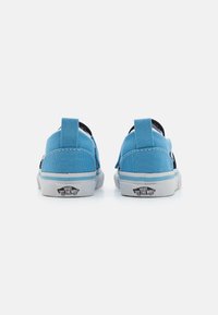 Blå canvas slip-on skor med svarta accenter, vit foder och grå gummisula. Varumärke visas på hälen. Bakifrån.