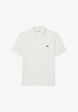 Valkoinen puuvillapaita, jossa on kaulus, kolme nappia ja pieni brodeerattu krokotiililogo vasemmassa rintapielessä.