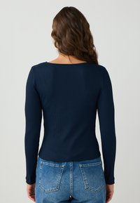 Langsleeve ribbeltop in donker marineblauw, met een ronde halslijn en een getailleerde silhouet. Gepaard met high-waisted blauwe denim jeans.
