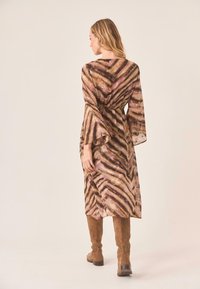 Vestido de manga larga con un patrón ondulado en marrón, rosa y crema, ceñido en la cintura, con mangas acampanadas. Botas de ante marrones hasta la rodilla.