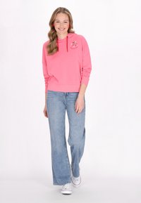 Felpa rosa con coulisse e ricami floreali, abbinata a jeans a gamba larga blu chiaro e sneakers bianche. Tessuto morbido.