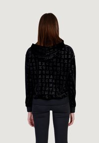 La sudadera de terciopelo negro presenta un patrón texturizado con el logotipo "ARMANI EXCHANGE", una capucha amplia y puños y dobladillo acanalados. Corte estándar.