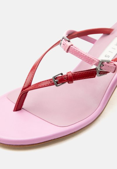 Ροζ σανδάλι με λεπτά κόκκινα και ροζ δερμάτινα λουράκια και ασημένιες αγκράφες σε επίπεδη σόλα σε λευκό φόντο.