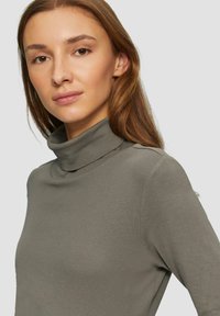Langsleeve, olijfgroene coltrui gemaakt van een zachte, rekbare stof. Heeft een aansluitende kraag en een gladde textuur.