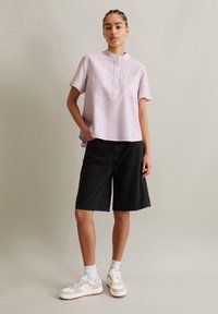 Lichtroze gestreepte kortom mouw shirt met een ronde kraag, gecombineerd met zwarte denim shorts en witte sneakers met crèmekleurige accenten.