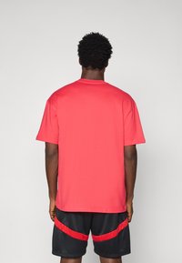 Rød bomulds T-shirt med korte ærmer, rund halsudskæring og en afslappet pasform, parret med sorte mesh shorts med røde accenter.