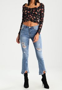 Svart blommig cropped topp med långa ärmar och volangkant, matchad med ljusblå slitna jeans med råa kanter och rivna detaljer.