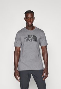 Camiseta gris con el logo "THE NORTH FACE" en negro, escote redondo, mangas cortas y un material de algodón suave y ligero.