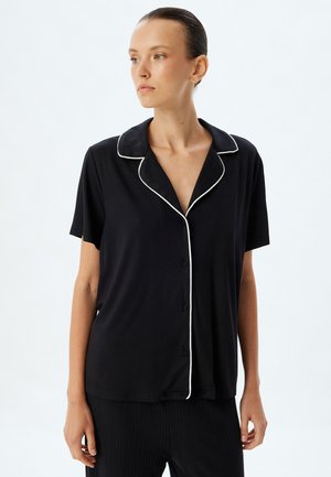 Zwarte shirt met korte mouwen en een notched collar, met witte piping, met een knoopsluiting aan de voorkant en een ontspannen pasvorm. Zacht, glad materiaal.