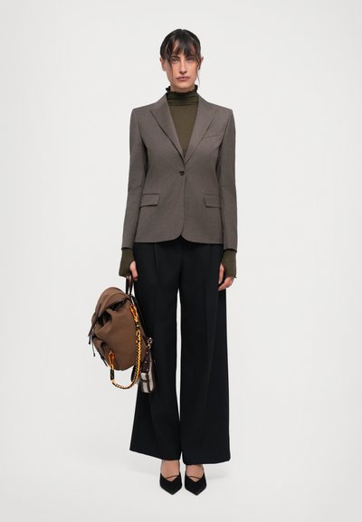 Grå skræddersyet blazer, olivengrøn turtleneck, sorte vidde bukser, sorte spidse hæle, holder en brun taske med kædeudsmykninger og en lille pung.