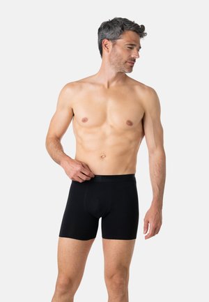 Boxer noir fabriqué en tissu lisse et extensible. Il présente une ceinture douce et une coupe ajustée, s'étendant jusqu'au milieu de la cuisse.