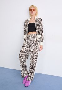 Leopard print tracksuit in beige and brown, with a white stripe. Accompanied by purple sneakers and round, tinted sunglasses.