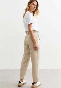 Beige, op maat gemaakte broek met een hoge taille en zijzakken. Gecombineerd met een plain wit t-shirt en witte sneakers met zwarte accenten.