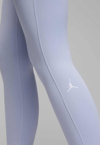 Leggings de color púrpura claro hechos de tela elástica, con una textura suave y un logo blanco de Jumpman en la parte superior del muslo.