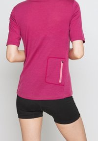 Fialová košile s krátkým rukávem s texturovaným povrchem, se zipovou kapsou na zadní straně v růžové barvě, spárovaná s černými šortkami.