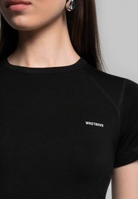 Black fitted t-shirt made of smooth fabric, featuring a crew neck and short sleeves. White logo "WRSTBHV" on left chest area.