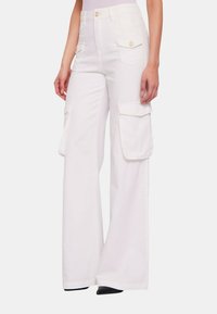 Pantaloni cargo bianchi con gambe larghe, due tasche laterali e un design a vita alta. Realizzati in denim con una texture liscia e bottoni dorati.