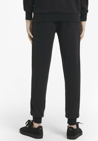 Černé tepláky vyrobené z měkké látky, zúžené na kotnících s žebrovanými manžetami. Nosí se s černými semišovými teniskami se zlatými akcenty.