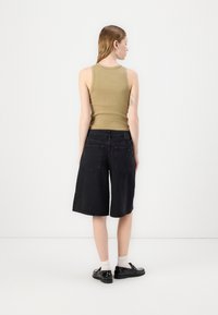 Fitted beige tank top and black denim culottes, featuring two back pockets, with black shoes and white socks. Backview against a plain background.