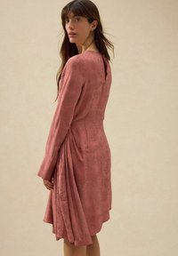 Dammig rosa klänning med långa ärmar, texturerad tyg med bladmönster, strukturerad liv, och en draperad kjol med detalj bak.