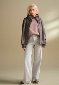 Bruine geruite waterdichte jas over een lichtroze sweatshirt, gecombineerd met lichtgrijze wijde jeans en bruine schoenen. Eenvoudig, casual ontwerp.