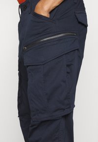 Marinblå cargobyxor med en ficka med dragkedja, flera sidfickor och ett slitstarkt tyg med en mjuk yta.