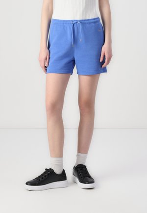 Shorts en coton bleu avec cordon de serrage, présentant une texture légère et une taille côtelée. Associés à des baskets noires et des chaussettes gris clair.