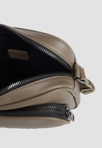 Braune Lederhandtasche mit strukturiertem Finish, ausgestattet mit einem schwarzen Reißverschluss und silbernen Hardware-Details, teilweise geöffnet, um das Innere zu zeigen.