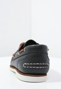 Chaussure en cuir bleu foncé avec des accents marron et des œillets dorés. Semelle intermédiaire blanche et détails de couture. Logo Timberland au niveau du talon.